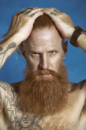Confident adult red haired hipster touching hair and looking at camera