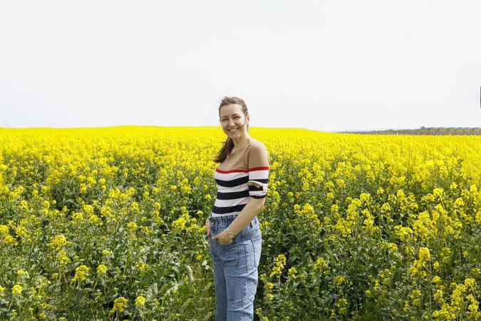 Smiling woman in jeans in yellow field on overcast day