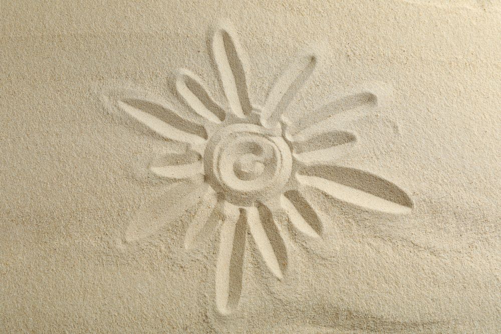 Sun drawing on clear sea sand, space for text and top view. Summer vacation background