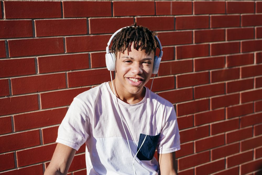Young happy Black male listening music with smartphone on bike