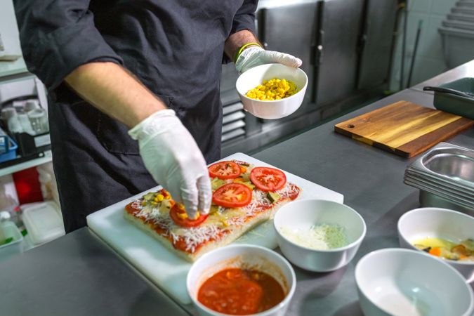 Anonymous male chef preparing vegetarian pizza with healthy ingredients in a restaurant kitchen