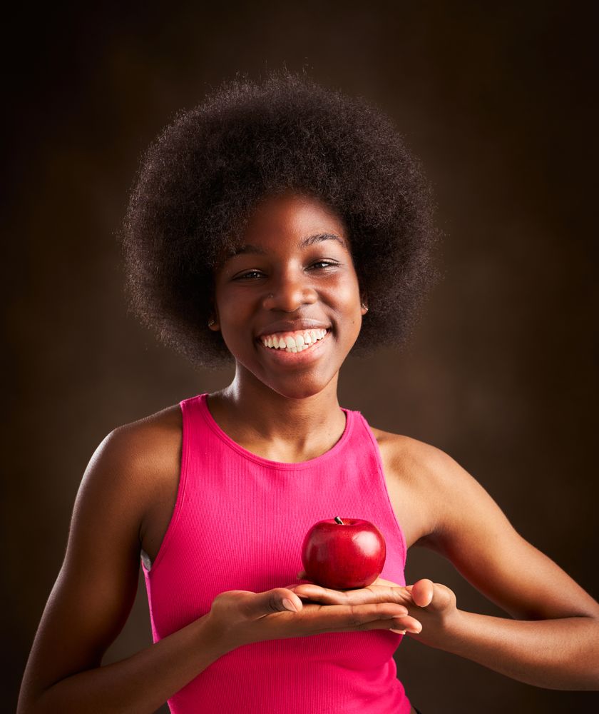 young woman with afro hairstyle happy with an apple in studio