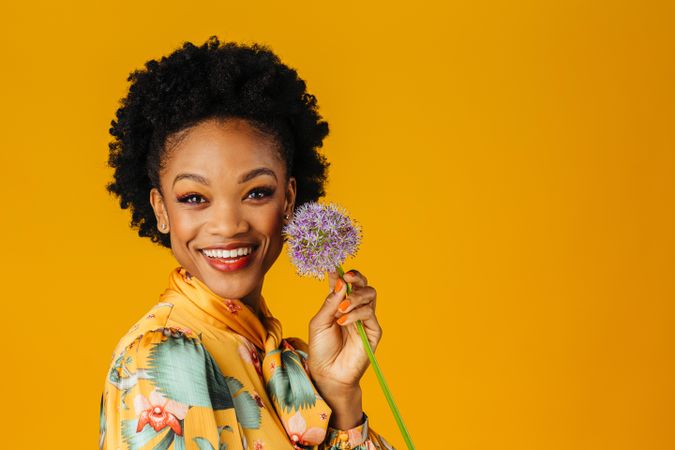 Happy Black woman holding purple flower to her face