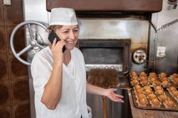 Baker woman speaking on the phone in front of the oven after preparing some cupcakes