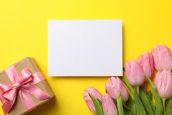 Pink tulips, gift box and empty place on yellow background, space for text