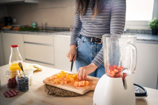 Crop woman cutting fruits for smoothie