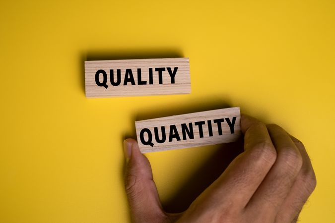 male hand holding quality and quantity words on wooden blocks isolated on yellow background