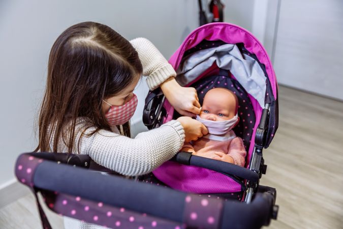 Girl with face mask putting mask on her baby doll