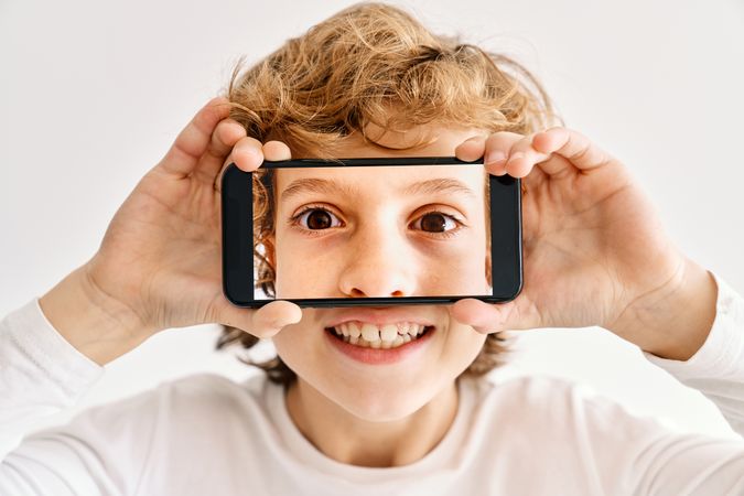Child posing with his mobile phone and photos made of parts of his face
