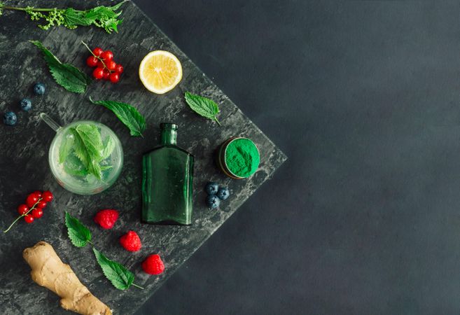 Healthy scene of spirulina powder, nettle leaves, berries, ginger on marble slap on dark background