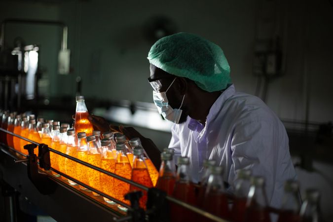 A factory worker is holding a bottle of fruit juice to inspect its quality inside a beverage manufacturing facility.