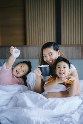 Mother having her morning coffee with children on bed 428qg0