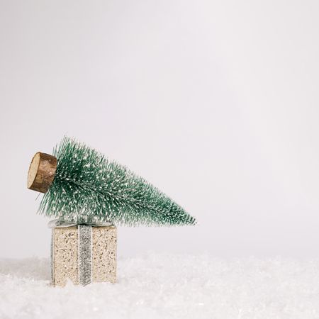 Miniature holiday tree on wrapped golden present on snowy scene