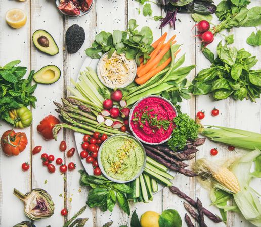 Fresh colorful vegetables and dips with hummus, avocados, asparagus, carrots on wooden table