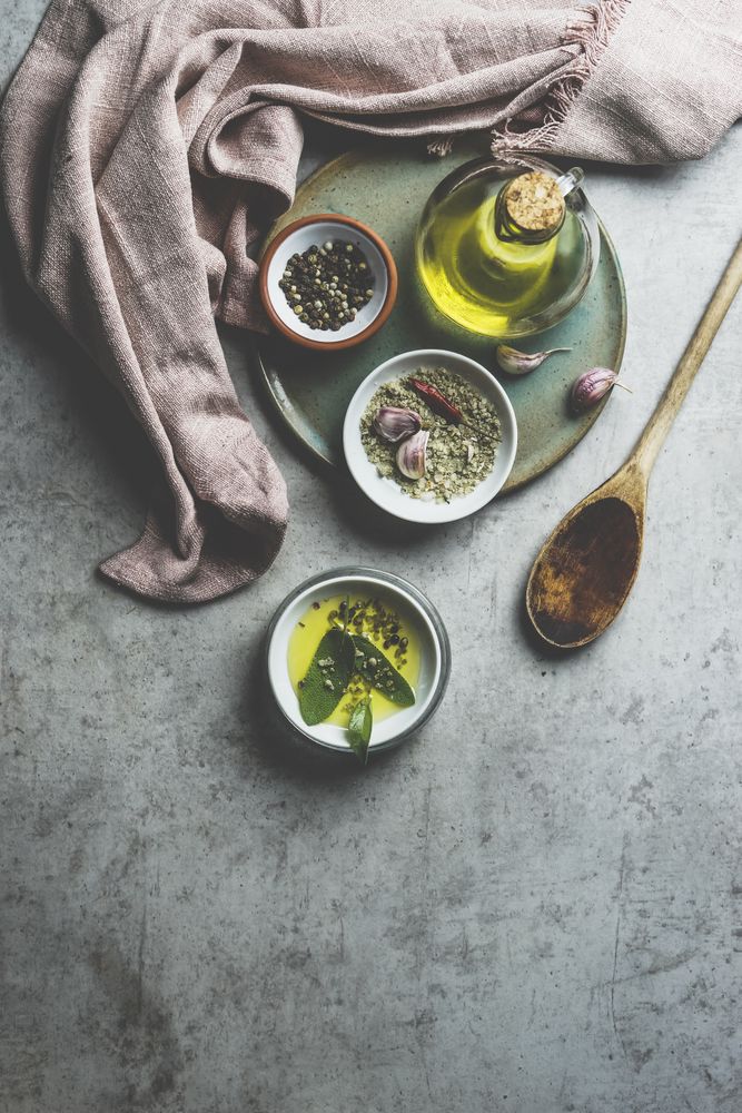 Healthy cooking ingredients on grey concrete kitchen table: olive oil, sage, garlic, pepper, salt, wooden cooking spoon, dish cloth