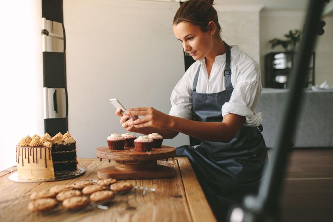 Female baker capturing photos of pastry items with her cell phone