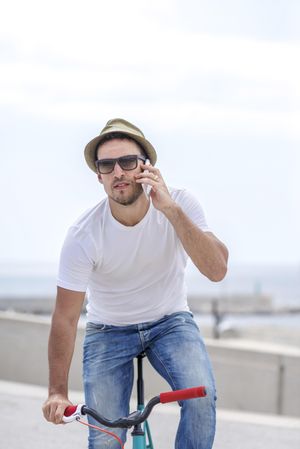 Male in hat riding bicycle outside using phone