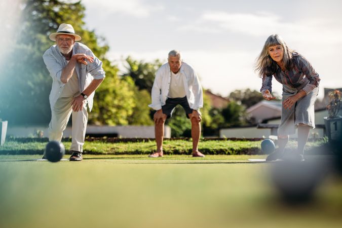 Ground level shot of man and woman playing boules in a lawn with a blurred boules in the foreground