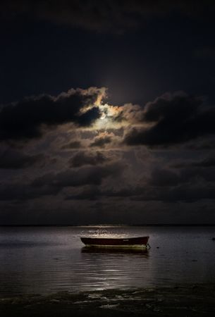 Full moon behind clouds above an ocean with a boat