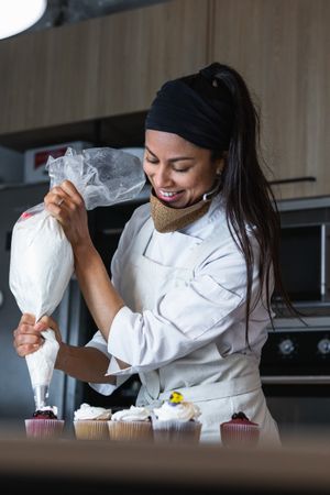 Female cook decorating cupcakes with whipped cream
