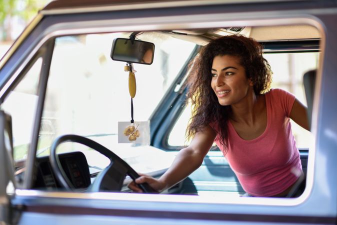 Smiling female in pink t-shirt with curly hair sitting up in passenger side of car