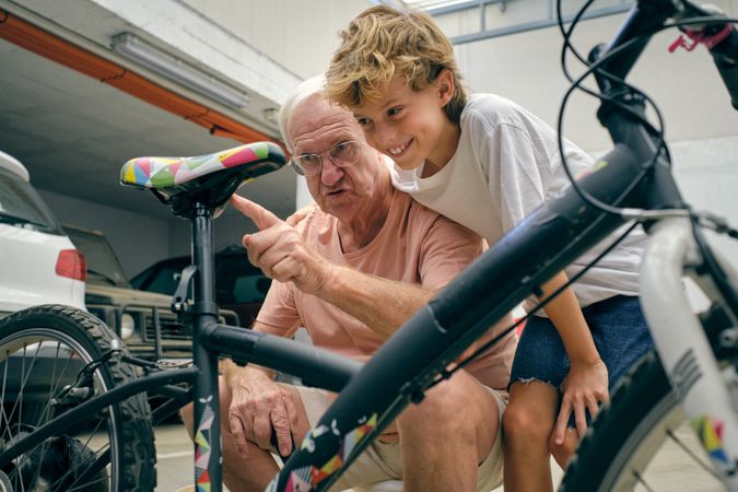 Mature man pointing at bicycle seat while talking to grandson