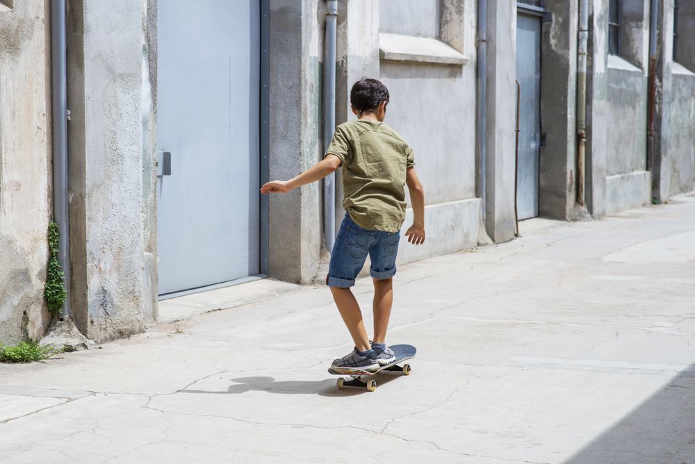 Back of a skater boy riding on the street on a sunny day