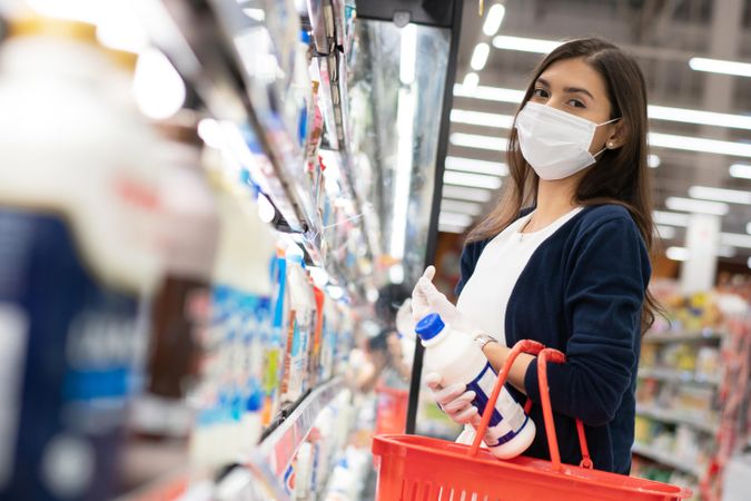 Woman placing items in basket at grocery shopping in surgical mask