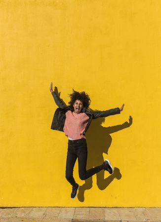 Black woman with afro hair jumping for joy in the street.