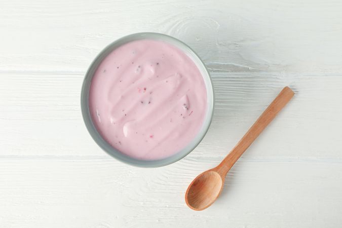 Fruit yogurt in bowl and spoon on wooden background