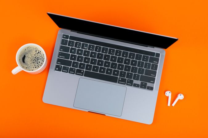 Top view of laptop on orange desk with mug of coffee or tea and ear buds