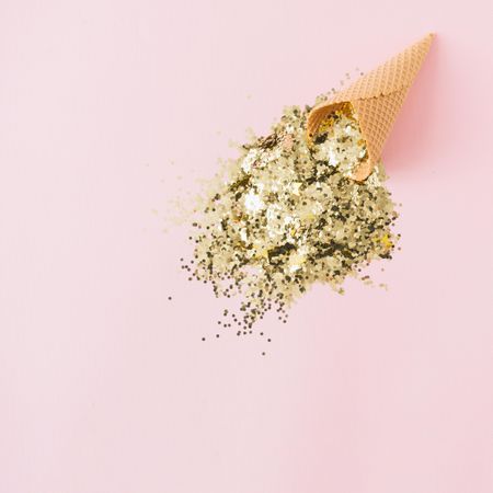Ice cream cone with gold glitter on pastel pink background