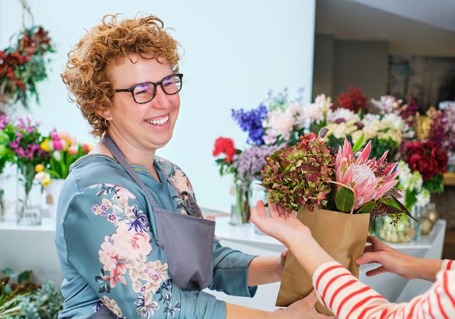 Smiling female florist giving bouquet to client