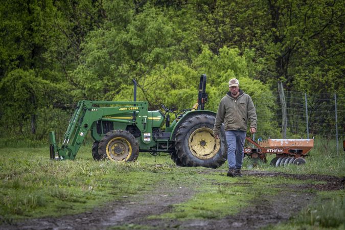 Copake, New York - May 19, 2022: Farmer walking away from tractor in field