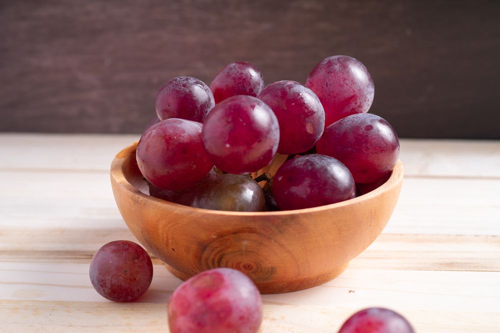A bowl of red grapes sits on a wooden table