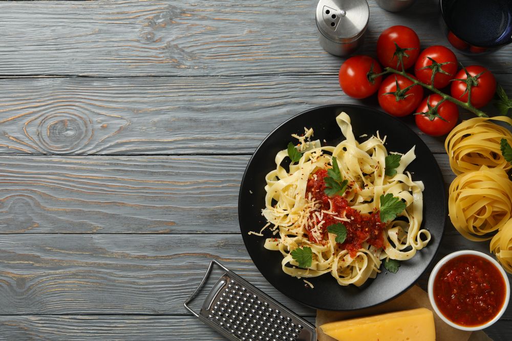 Composition with plate of tasty pasta and ingredients for cooking on wooden background