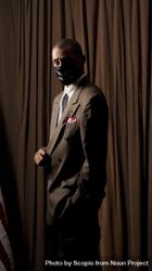 Man in brown suit with facemask standing 5kw165