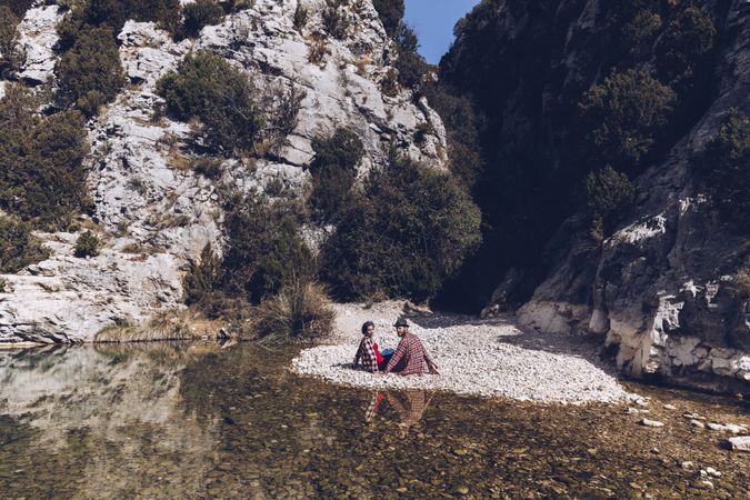 Positive woman and man resting on stone shore near river