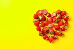 Flat lay composition with strawberries in the shape of heart on color background, space for text