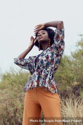 Black woman in colorful patterned top and brown pants standing bEX9A4