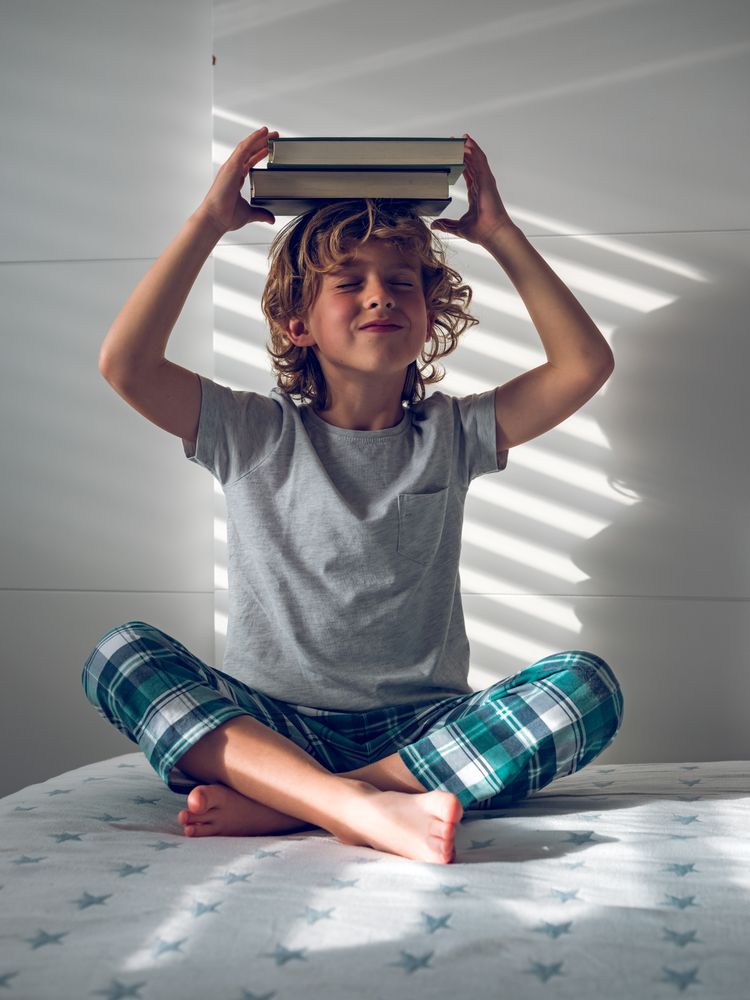 Little boy putting pile of books on head