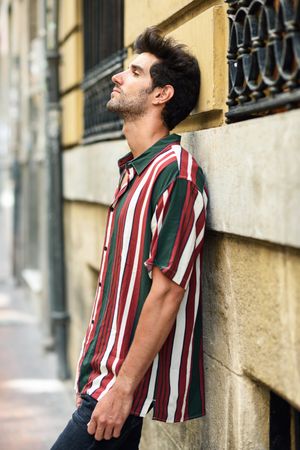 Side view of dark haired man leaning on wall outside