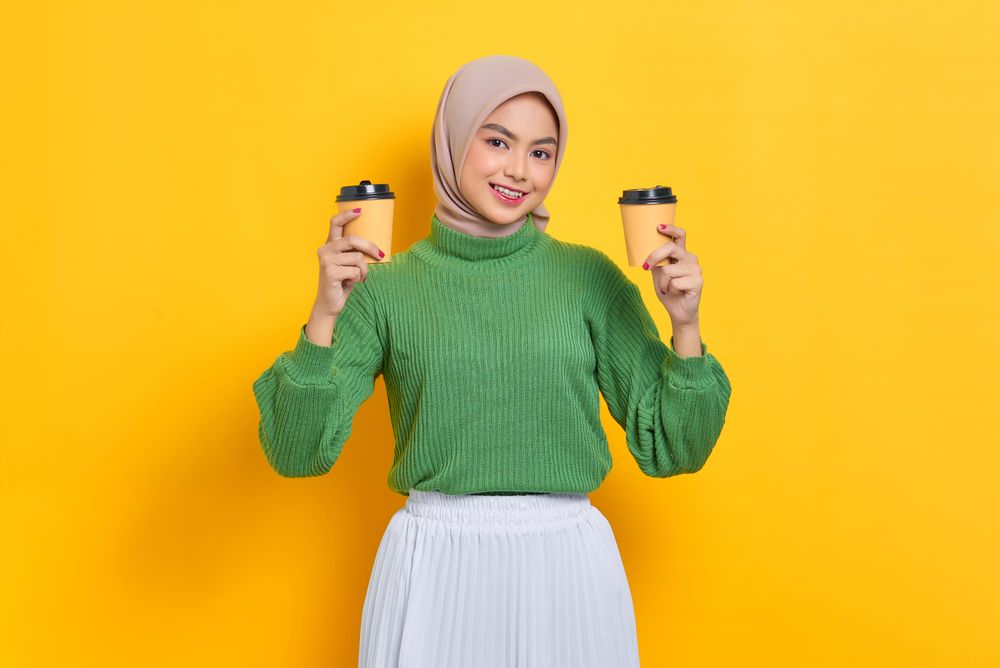 Woman in headscarf holding two to go coffee cup