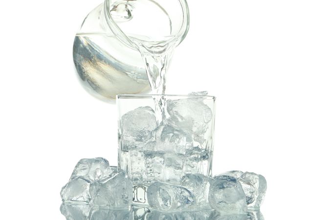 Pitcher of water being poured into glass surrounded by ice