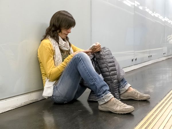 Woman sitting on ground of subway station using phone