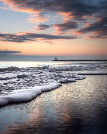 Wide shot of calm sea waves crashing on shore during sunrise under clouds