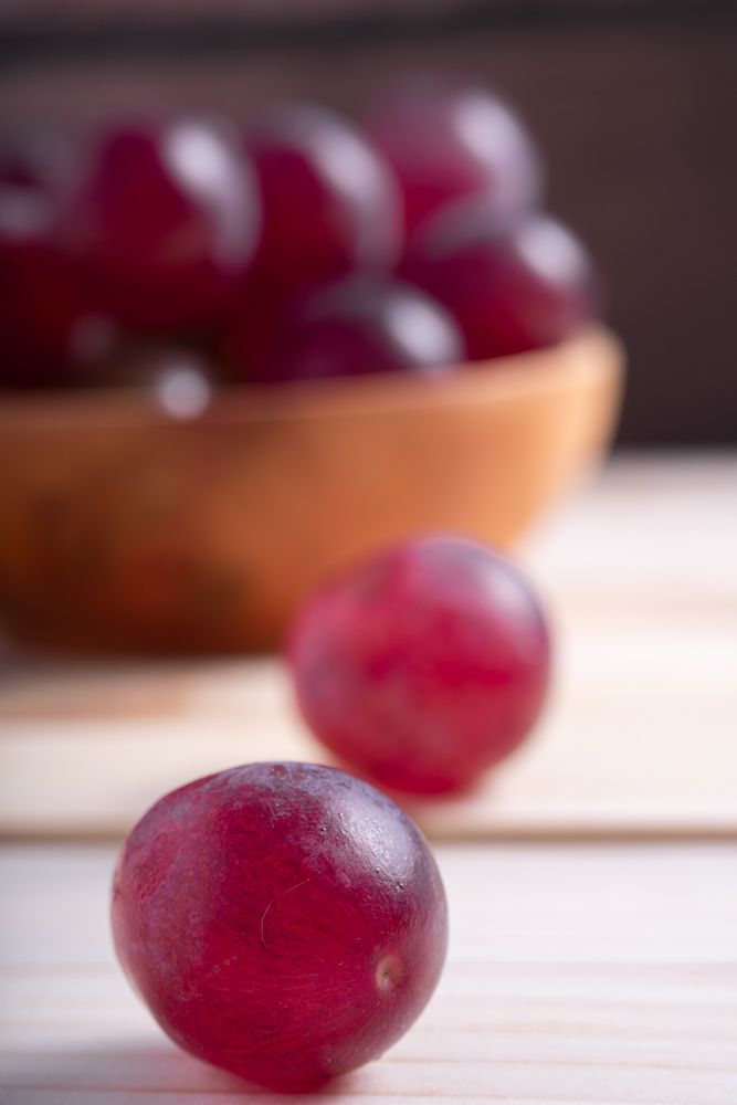 A bowl of red grapes sits on a wooden table
