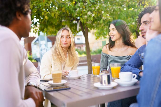 Diverse friends having a conversation over coffee and juice at outside table