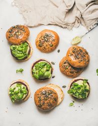 Fresh vegan burgers on seeded buns arranged on light background