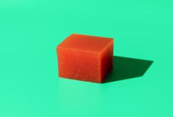 Cube of quince jelly for cheese plate on bright green background